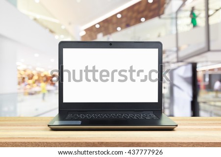 Laptop computer isolated blank white screen on wood table with blurred modern fashion shopping mall background