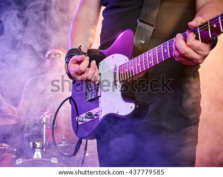 Rock band performs on stage. Guitarist, bass guitar and drums. Guitarist in the foreground. Close-up. Royalty-Free Stock Photo #437779585