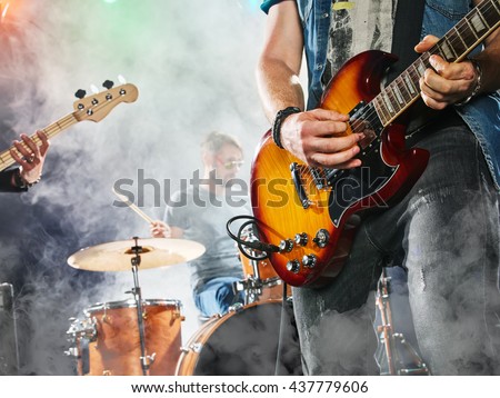 Rock band performs on stage. Guitarist, bass guitar and drums. Guitarist in the foreground. Close-up. Royalty-Free Stock Photo #437779606