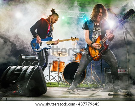 Rock band performs on stage. Guitarist, bass guitar and drums. The guitarist plays solo. Royalty-Free Stock Photo #437779645