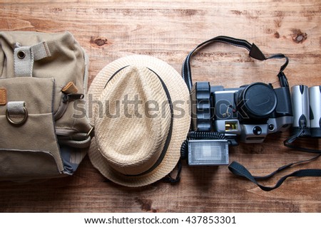 Tourism concept. Backpack, hat , binocular and old camera isolated on wooden background.