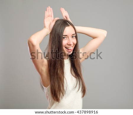 Funny girl showing bunny ears with her hands isolated on gray background