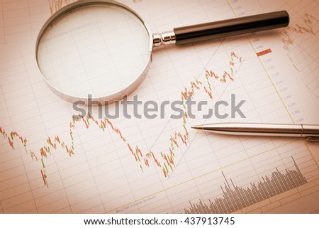 Vintage / retro color style : Blue ballpoint pen and a magnifier on a chart of financial instruments for stock / equity technical analysis. Charts include volume analysis, candlestick trend signal. Royalty-Free Stock Photo #437913745