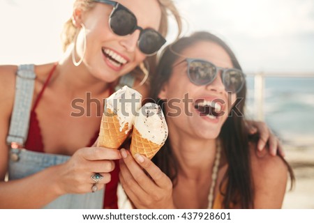 Two young female friends having fun and eating ice cream. Cheerful young women eating icecream outdoors. Royalty-Free Stock Photo #437928601