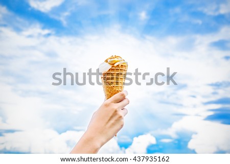 girl hand holding ice cream up to blue sky and clouds