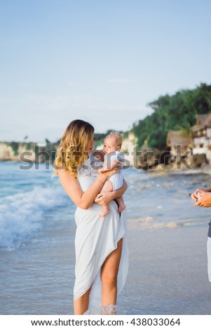 young smiling mother in flying white dress with her baby on the beach . Mother holds newborn baby in her arms . Happy woman with a child smiling and kissing her baby. close up portrait out door