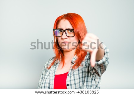 closeup of red-haired girl shows her dislike, thumbs down, wears glasses