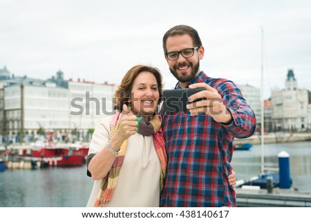 Mother and son taking selphie picture at an urban harbour doing success thumbs up sign. Family on vacations.
