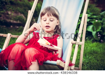 young mannered fashion girl in red dress relaxing in chaise lounge eat cake during outdoor party in the garden Royalty-Free Stock Photo #438146338