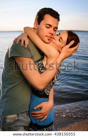 Happy beautiful young couple walking and embracing on the beach of the sea at summer sunset. Concept of the love and family, summer holiday, vacation, travel.