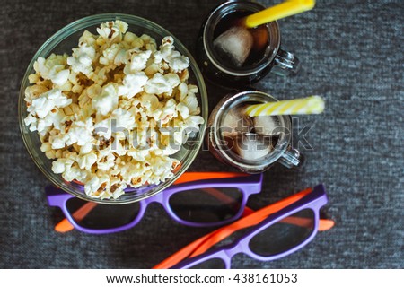 Cola with ice, popcorn in a clear bowl and 3D glasses
