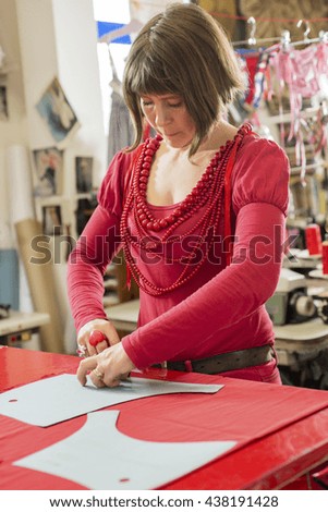 A seamstress in red dress and necklaces tracing cloth