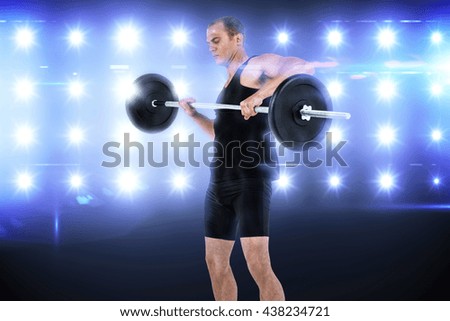 Bodybuilder lifting heavy barbell weights against composite image of blue spotlight