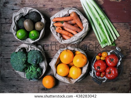 Mixed colorful fruits and vegetables  (orange, carrot, broccoli, celery, tomatoes, lemon, tomato cherry, blueberry and raspberry) in paper bag and basket creative draw on the wooden table Royalty-Free Stock Photo #438283042