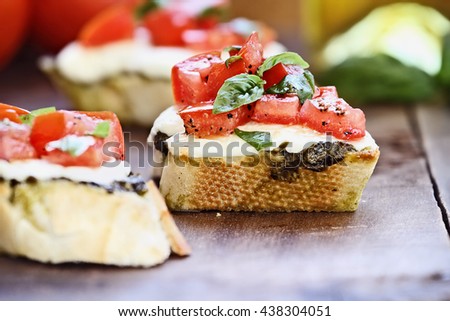 Bruschetta appetizers with tomato, mozzarella cheese, and pesto.  Extreme shallow depth of field and selective focus on center sandwich.