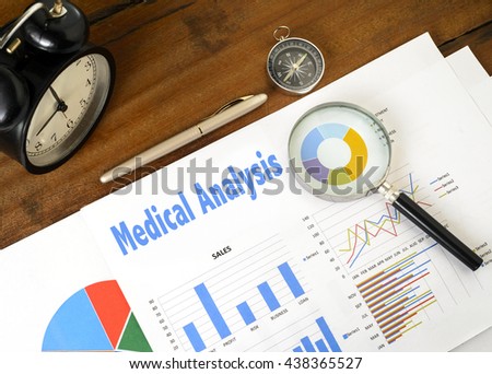 "Medical Analysis" text on paper sheet with magnifying glass on chart clock,compass, pen, on wooden table - business, banking, finance and investment concept