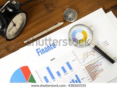 "Finance" text on paper sheet with magnifying glass on chart clock,compass, pen, on wooden table - business, banking, finance and investment concept