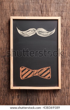 Hand drawn of mustache and bow tie on chalkboard with space for text on wooden table top. For greeting card, invitation card, birthday and father's day