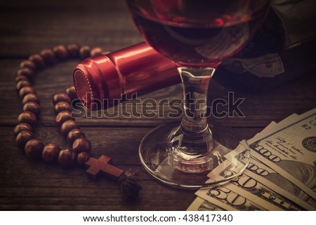 Bottle of red wine with a glass of red wine and money with rosary on an old wooden table. Close up view, focus on the glass of red wine, image vignetting and the yellow toning
