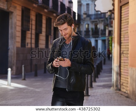 Young man listening music with smartphone earphones walking in the street