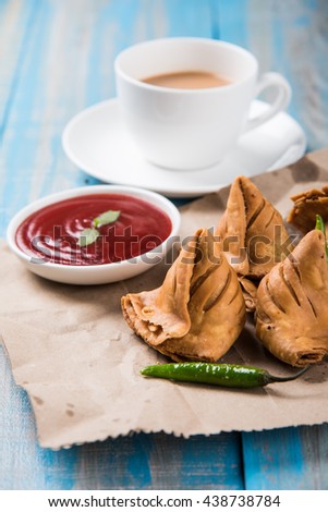 Veg Samosa - is a crispy and spicy Indian triangle shape tea time snack. Served with fried green chilly, onion & chutney/ketchup. Over colourful or wooden background. Selective focus