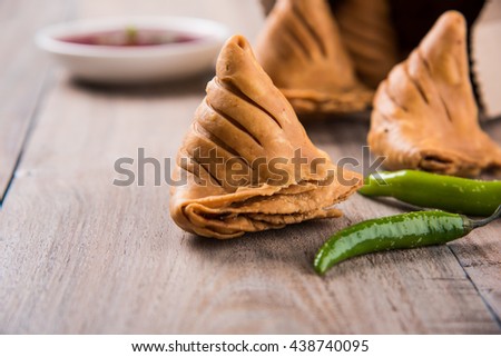 Veg Samosa - is a crispy and spicy Indian triangle shape tea time snack. Served with fried green chilly, onion & chutney/ketchup. Over colourful or wooden background. Selective focus