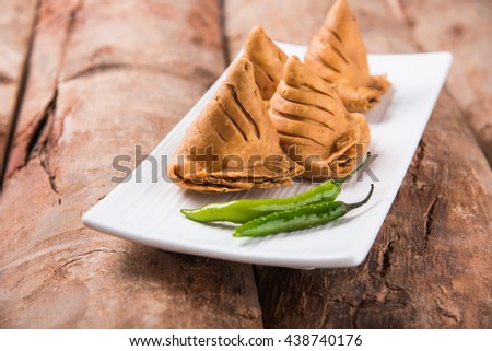 Veg mini Samosa - is a crispy and spicy Indian triangle shape tea time snack. Served with fried green chilly, onion & chutney/ketchup. Over colourful or wooden background. Selective focus