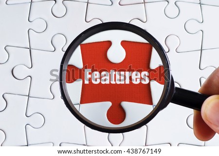 "Features" text on red missing jigsaw puzzle with man right hand hold black magnifying glass searching for missing puzzle peace - business and finance concept Royalty-Free Stock Photo #438767149