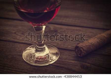 Glass of red wine and cuban cigar on an old wooden table. Close up view, image vignetting and the yellow toning