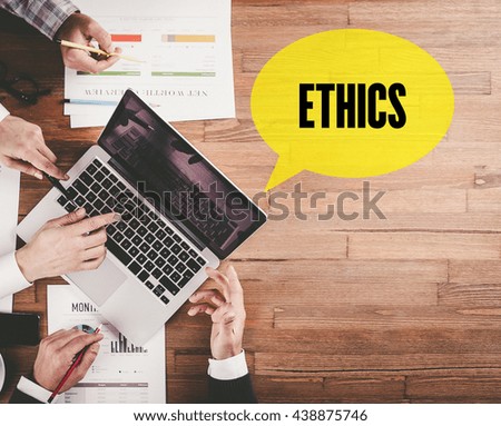 BUSINESS TEAM WORKING IN OFFICE WITH ETHICS SPEECH BUBBLE ON DESK