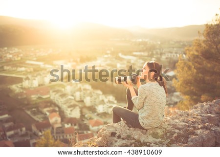 Female traveler photographer fascinated by illuminated nature at sunrise. Professional woman photographer taking outdoor portraits with telephoto lens. Taking break from job and enjoying the sunset.