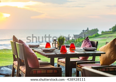 Outdoor dinner setting at sunset overlooking the coastline of a beautiful tropical Island. Royalty-Free Stock Photo #438928111