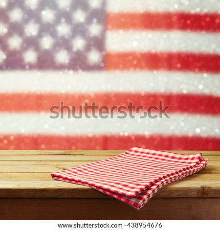 Empty wooden deck table with tablecloth over USA flag bokeh background. 4th of July celebration picnic background. Ready for product display montage.