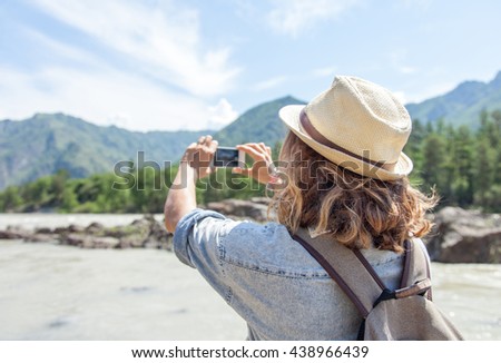 young woman traveler on a background of mountains takes photos on a mobile phone