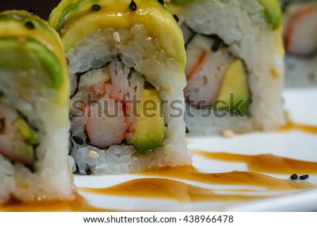 beautiful sushi roll topped with avocado stuffed with crab meat garnished with a sweet sauce and sesame seeds