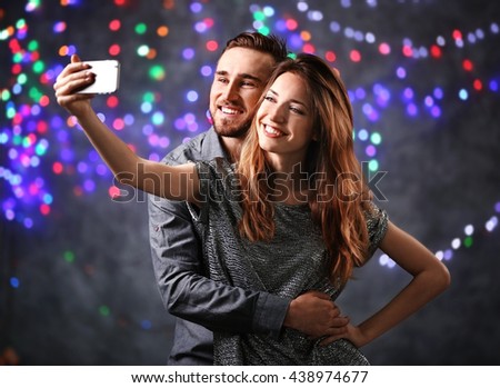 Young cheerful friends taking selfie on blurred colourful lights background