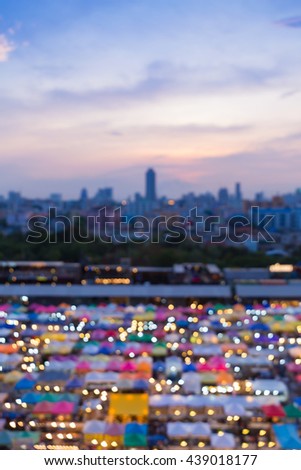Aerial view, blurred lights multiple colours weekend market with city downtown background