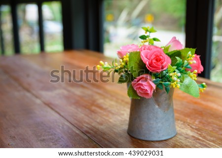 Pink roses in metal vase on wooden table by the window.