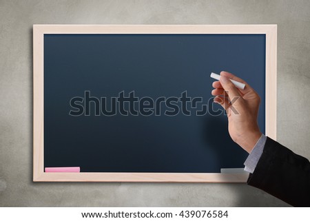 Business man hand holding white chalk with blank black chalkboard on concrete wall. Blank copyspace for your text or design. 