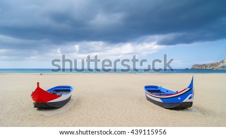 Traditional portuguese boats on the beach of the small touristic city Nazare, Portugal, summer day, after the rain Royalty-Free Stock Photo #439115956