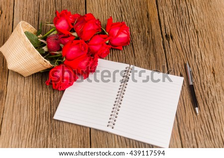 A photo of notepad on wood board with  red rose(Selective focus )
