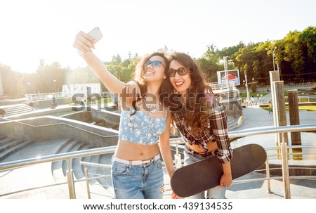 Young girls doing selfie with a skateboard. In the park