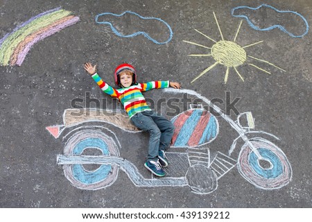 Happy little kid boy  in helmet having fun with motorcycle picture drawing with colorful chalks. Children, lifestyle, fun concept. child dreaming of future and profession.
