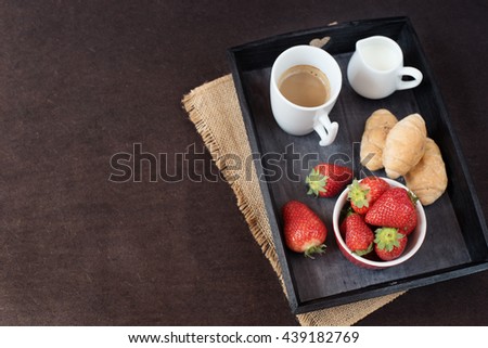 Coffee, mini French pastries and strawberries on wooden tray over black table. Black background
