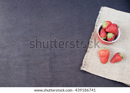 Fresh strawberries in mini red bowl on hessian jute. Black background. 
