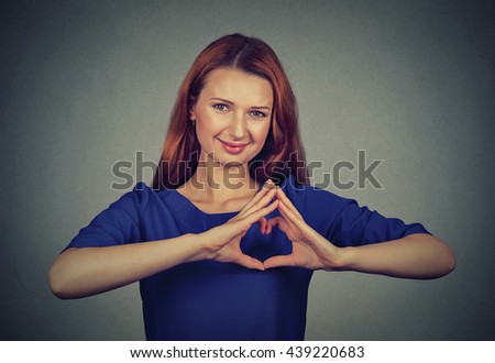 Closeup portrait smiling cheerful happy young woman making heart sign with hands isolated on gray wall background. Positive human emotion expression feeling life perception attitude body language