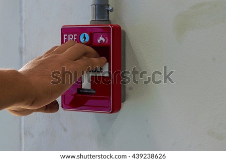 The hand of man is pulling fire alarm on the wall next to the door