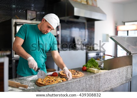 Chef cuts the freshly prepared pizza on a wooden substrate.