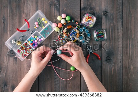 Making of handmade jewellery. Box with beads on old wooden table. Top view with woman hands Royalty-Free Stock Photo #439368382