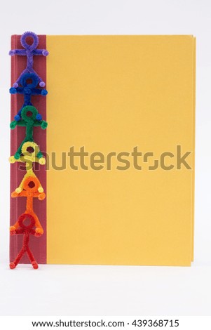 Rainbow pipe cleaner people stacked on each other for support against a yellow book. A simple educational photo great for a variety of ideas and concepts. Vertical with copy space.